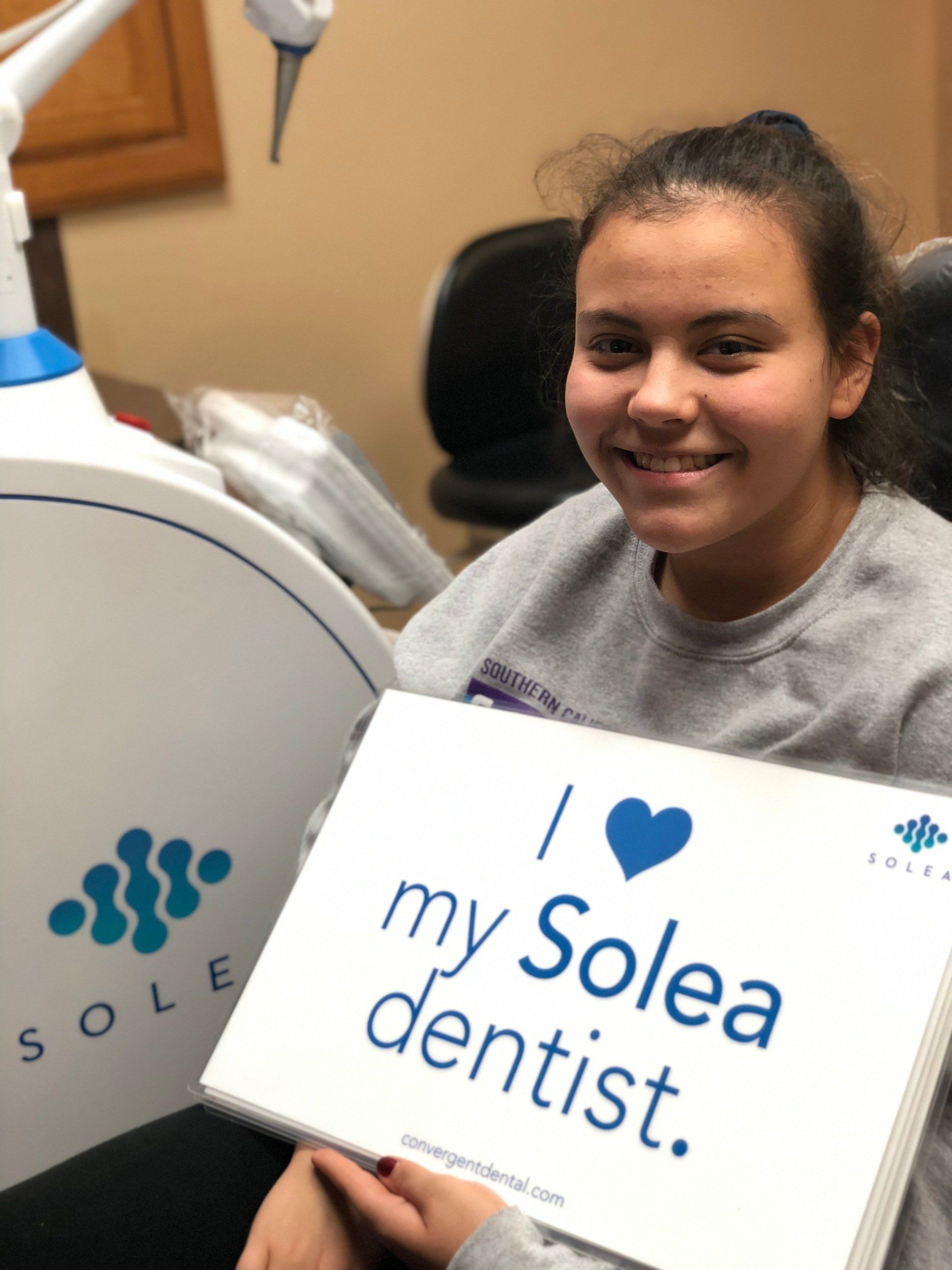 A girl holding a sign that says i love my solea dentist