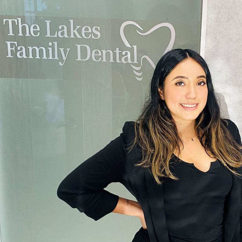 Ruby is standing in front of a sign for the lakes family dental .