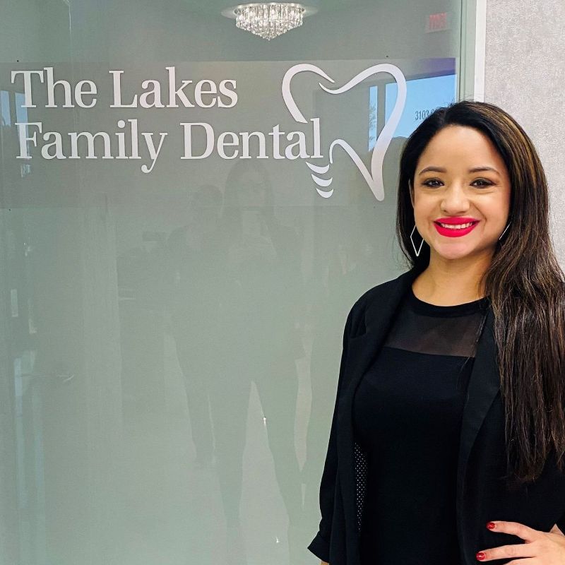 Chelsea is standing in front of a sign for the lakes family dental