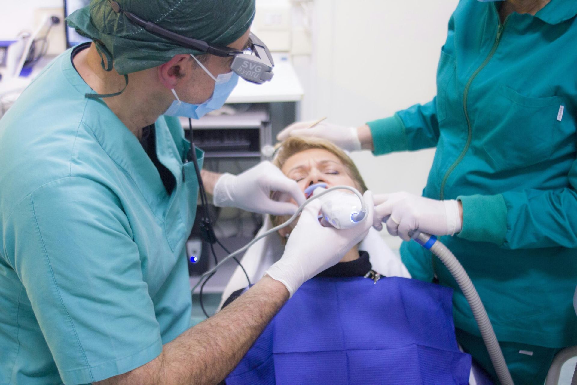Medical staff performing a dental procedure on a patient in a clinic, using surgical masks and gloves.