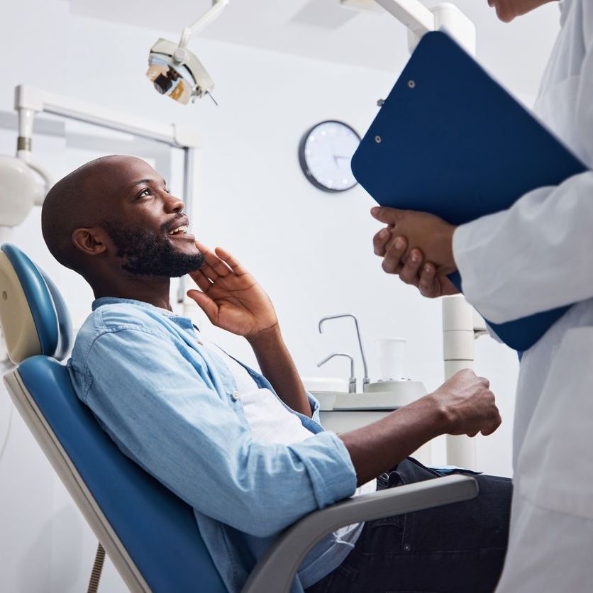 A man is sitting in a dental chair talking to a dentist