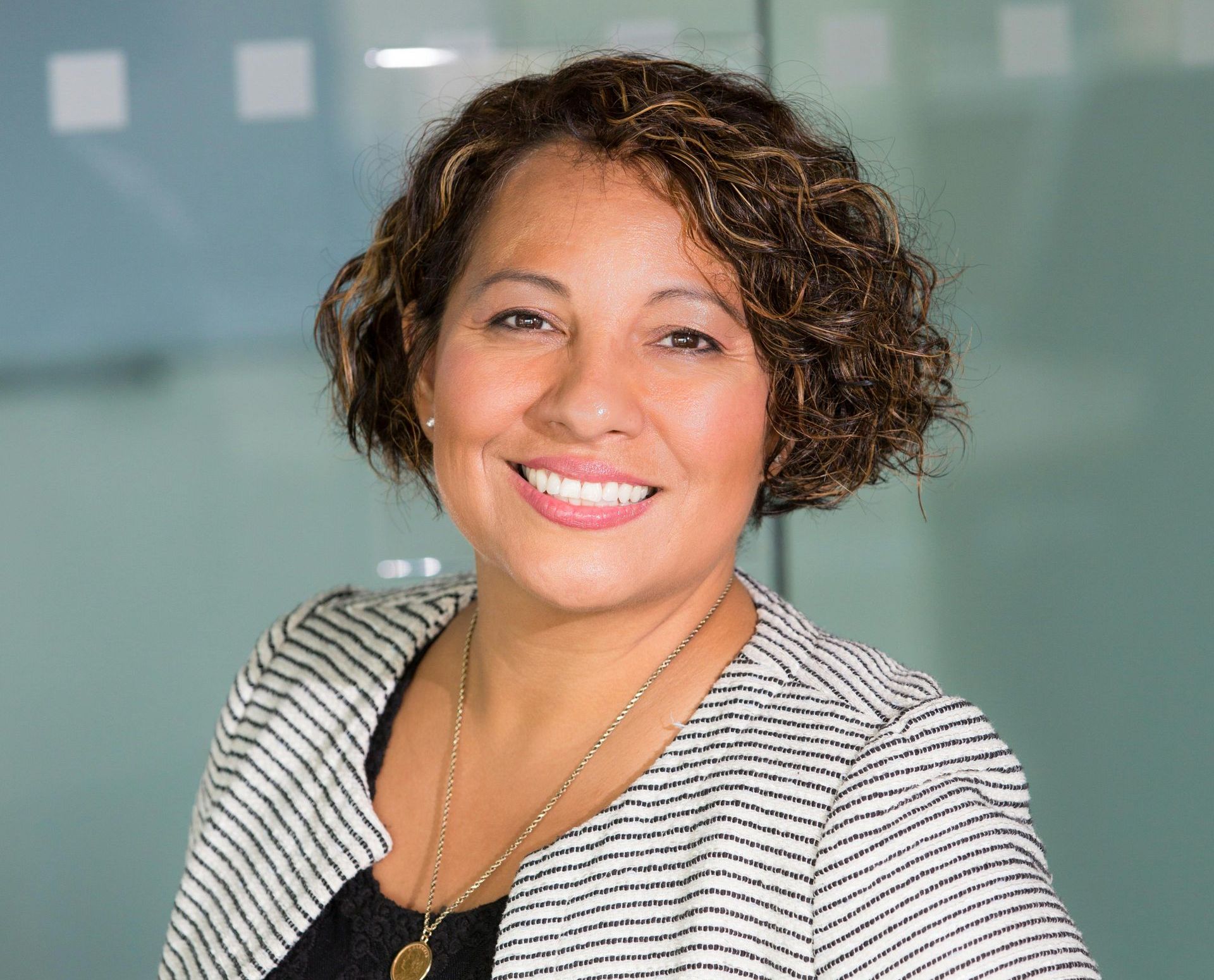 A woman with curly hair and a striped jacket is smiling for the camera.