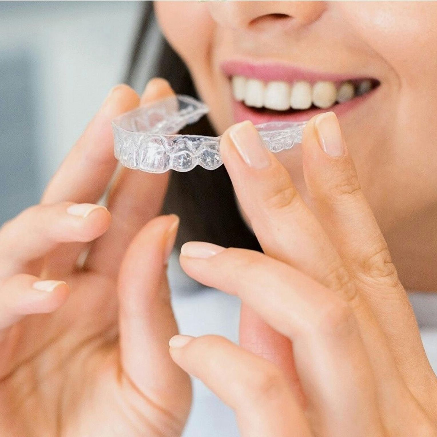 A woman is smiling while holding a clear retainer in her hands.