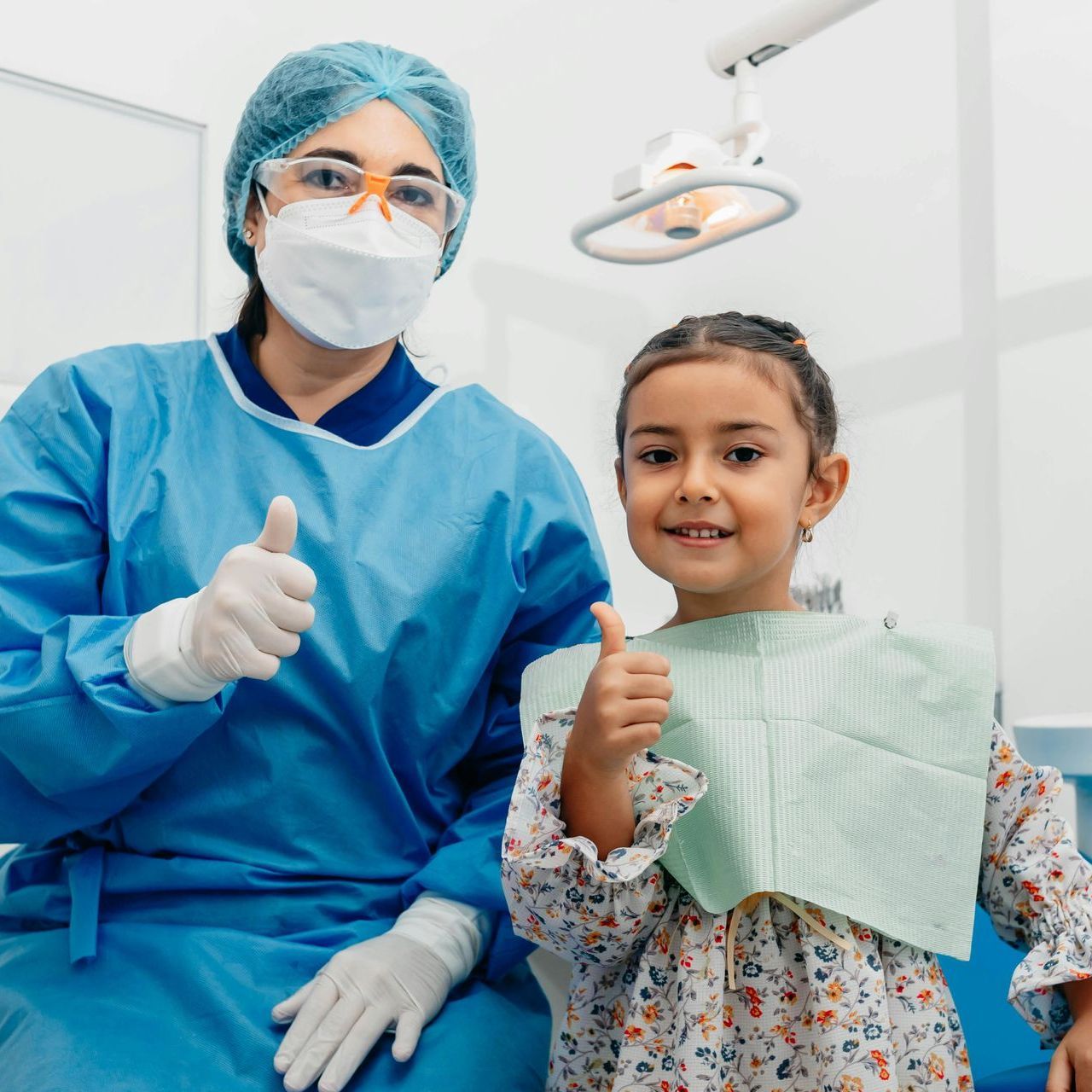 A little girl is giving a thumbs up next to a dentist.