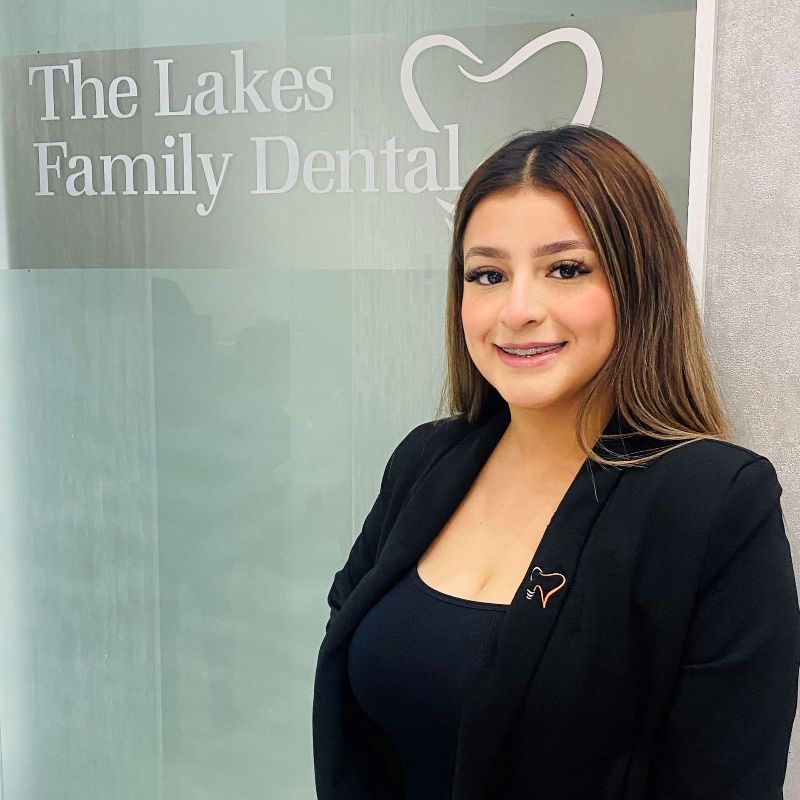 Frida is standing in front of a sign that says the lakes family dental .