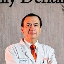 Man in a white coat and orange tie, possibly a dentist, standing in a dental office.