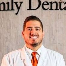 Dr. Rodriguez of The Lakes Family Dental, smiling in a white coat and orange tie, stands in front of the dental practice's logo.