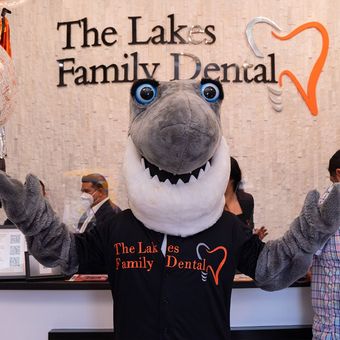 A shark mascot stands in front of a sign for the lakes family dental