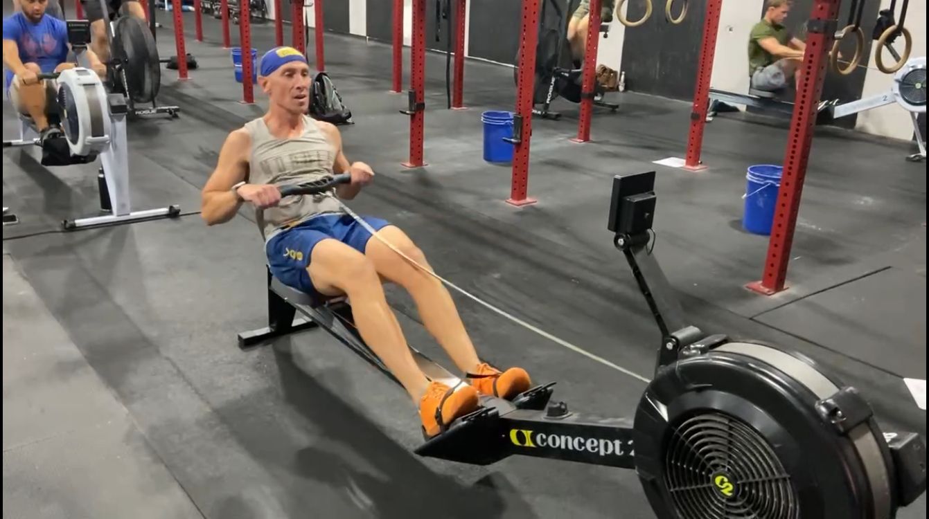A man is rowing a rowing machine in a gym.