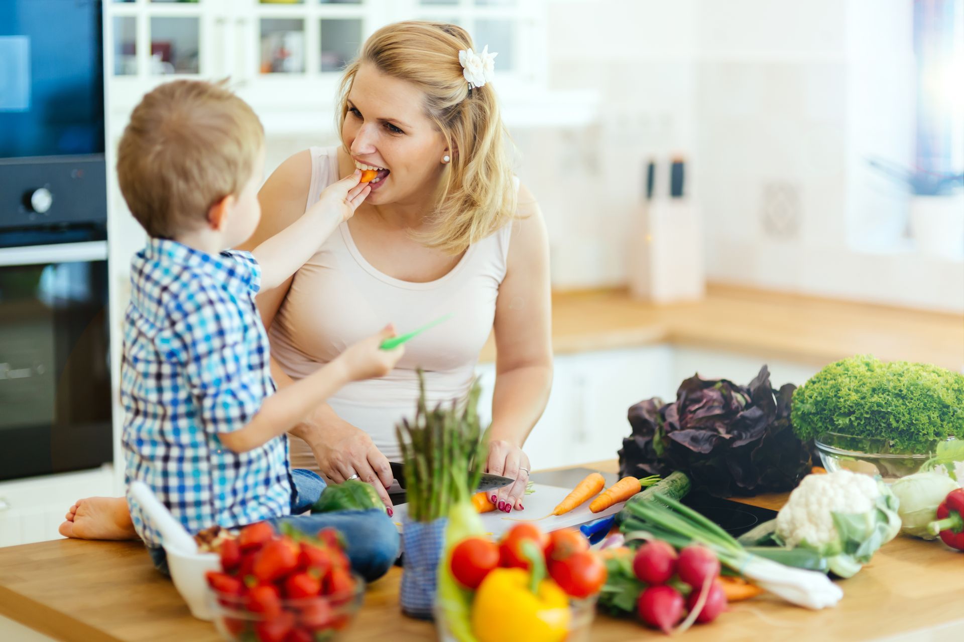 A woman and a child are eating vegetables in a kitchen.