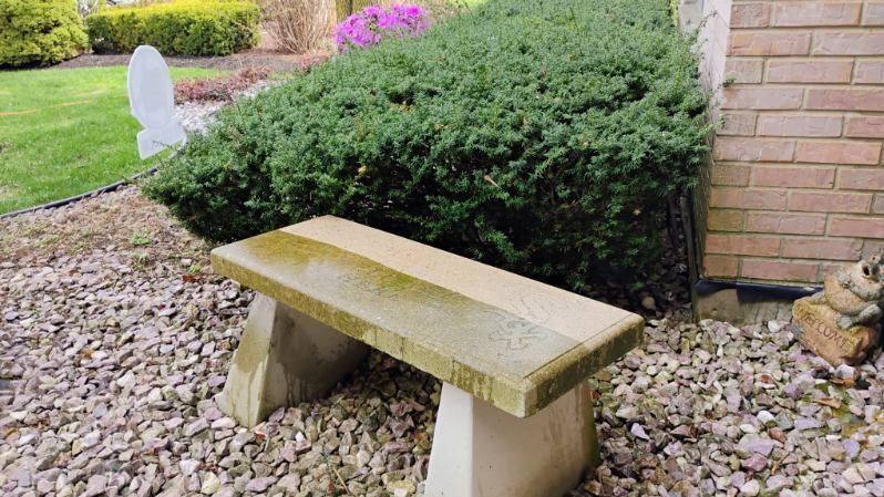 A stone bench is sitting in the gravel in front of a brick building.