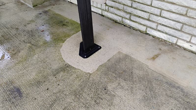A black pole is sitting on a concrete floor next to a white brick wall.