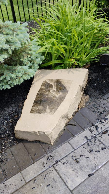 A large rock is sitting on top of a brick walkway next to a garden.