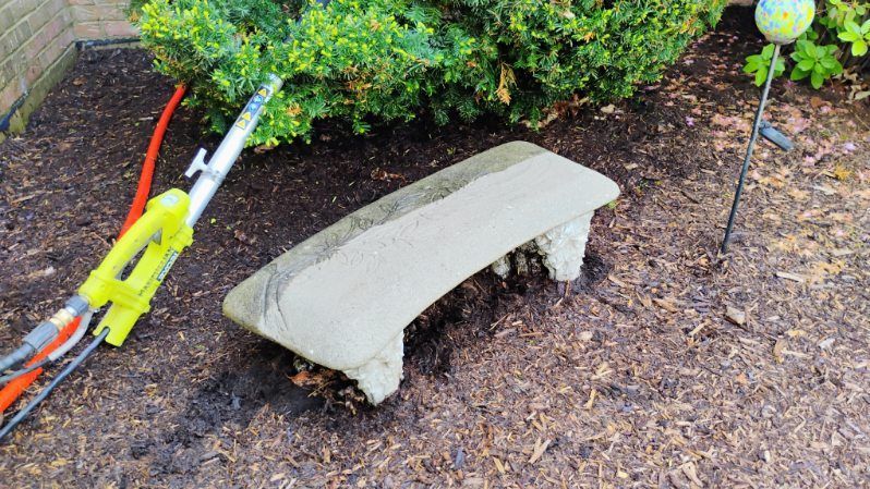 A stone bench is sitting in the middle of a garden next to a lawn mower.