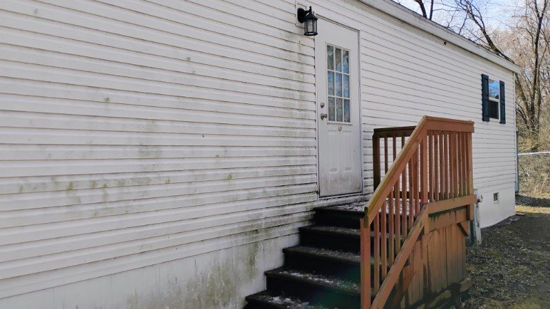 A white house with a wooden deck and stairs leading up to it.