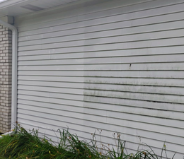 A person is using a high pressure washer to clean the side of a house.
