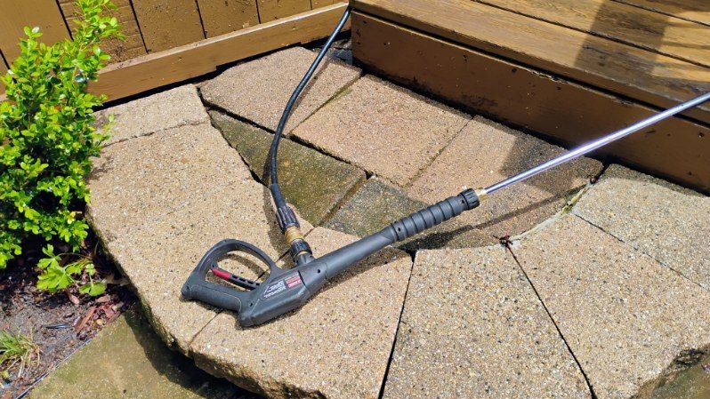 A high pressure washer is sitting on a brick patio next to a wooden deck.