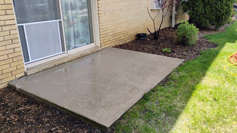 A concrete patio in front of a brick building with a sliding glass door.