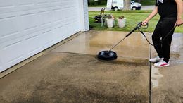 A person is using a high pressure washer to clean a sidewalk.