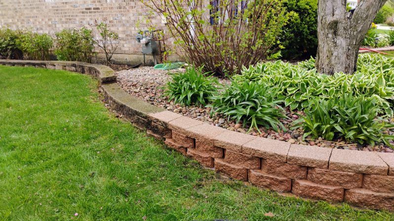 A brick wall surrounds a lush green lawn in a backyard.