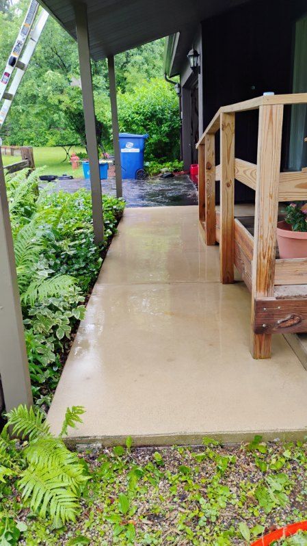 A concrete walkway leading to a porch with a wooden railing.