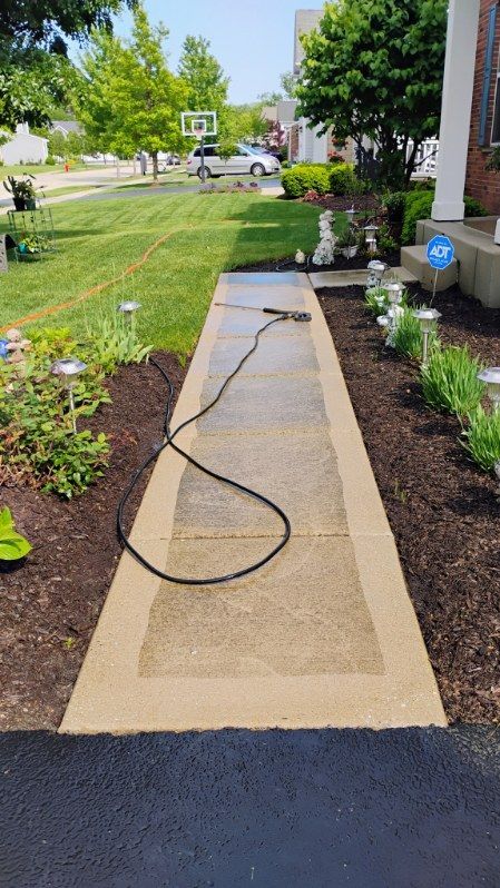 A sidewalk is being cleaned with a pressure washer.