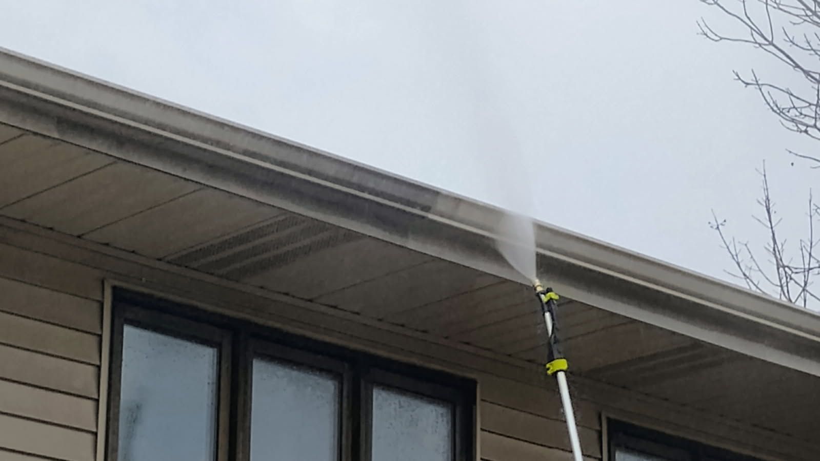 A person is cleaning the gutters of a house with a high pressure washer.