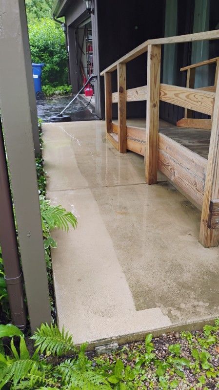 A concrete walkway with a wooden railing and stairs leading to a house.