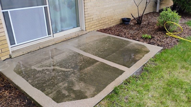 A dirty concrete patio next to a brick house with a yellow hose.