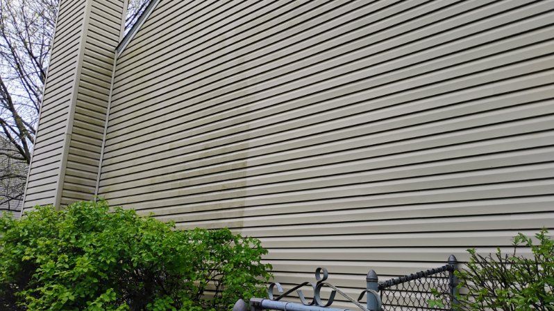 The side of a house with a fence and bushes in front of it.