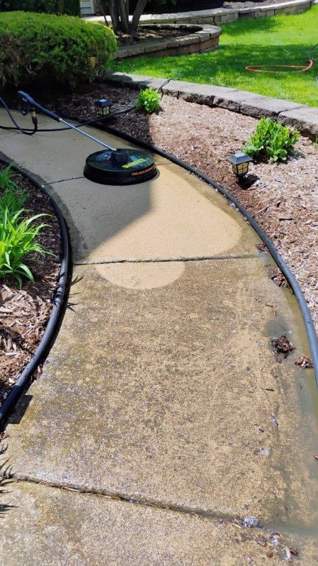 A concrete walkway is being cleaned with a pressure washer.
