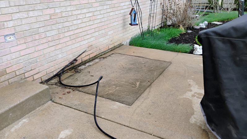 A hose is laying on the sidewalk next to a brick wall.