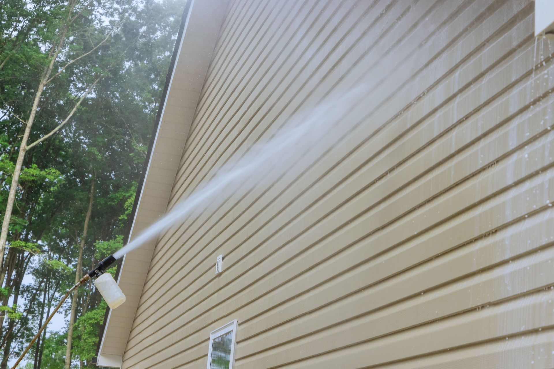 A person is using a high pressure washer to clean the side of a house.