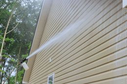 A person is using a high pressure washer to clean the side of a house.