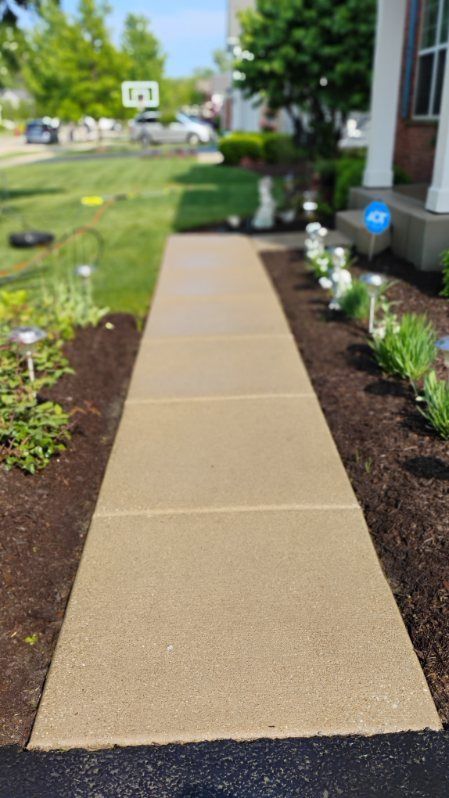 A sidewalk leading to a house with a garden in the background.