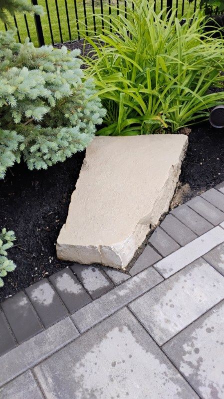 A large rock is sitting on top of a brick walkway next to a garden.