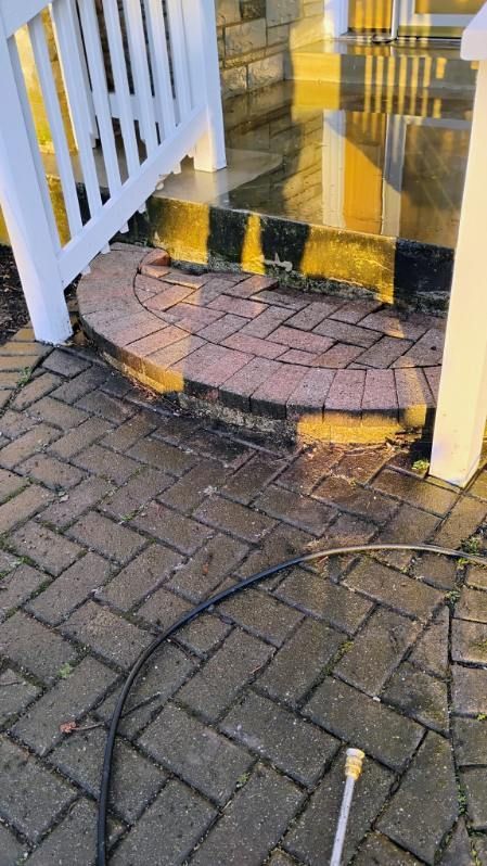 A person is cleaning a brick walkway with a high pressure washer.