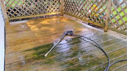 A person is using a high pressure washer to clean a wooden deck.