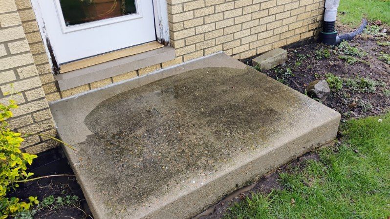 A dirty concrete step in front of a brick house.