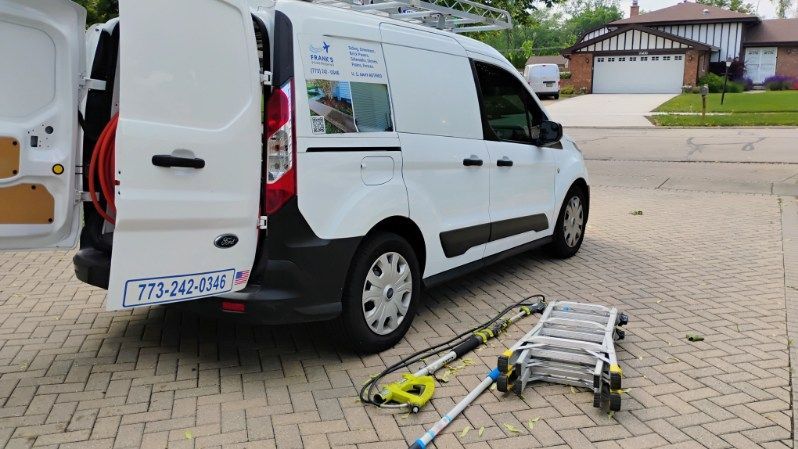 A white van is parked on a brick driveway next to a ladder.