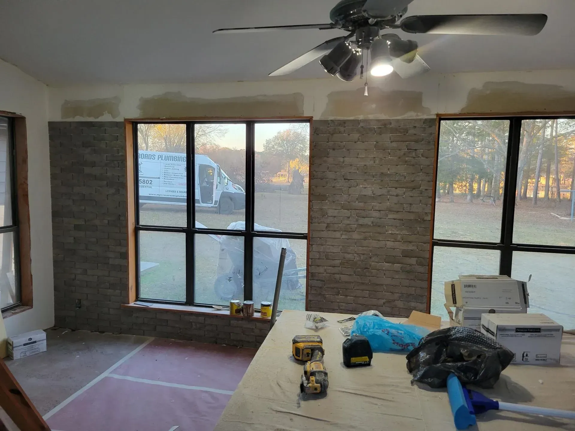 Interior room under construction, with windows and partially tiled walls. Tools and materials on a table.