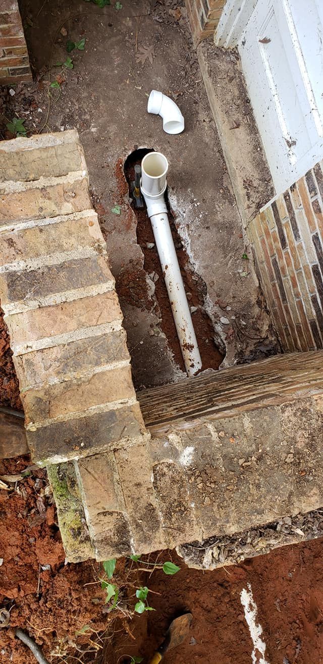 A white pipe is sitting in the dirt next to a brick wall.
