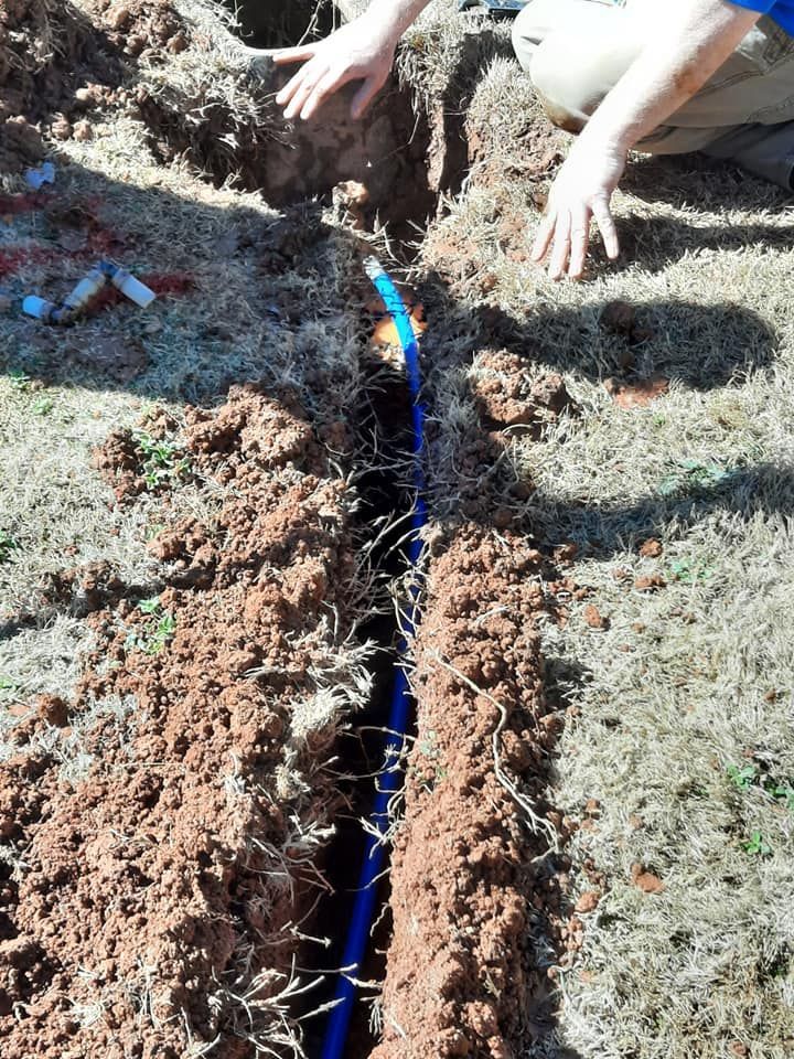 A person is kneeling in the dirt next to a blue pipe.