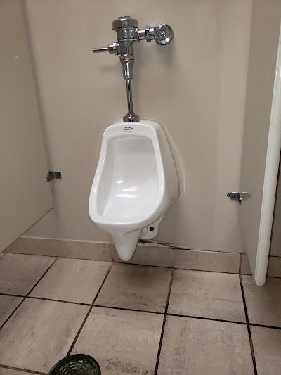 A white urinal is sitting on a tiled floor in a public restroom.