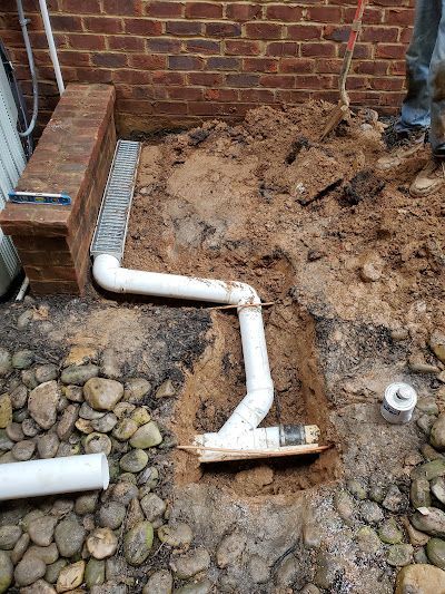 A man is digging a hole in the ground to install a drain pipe.