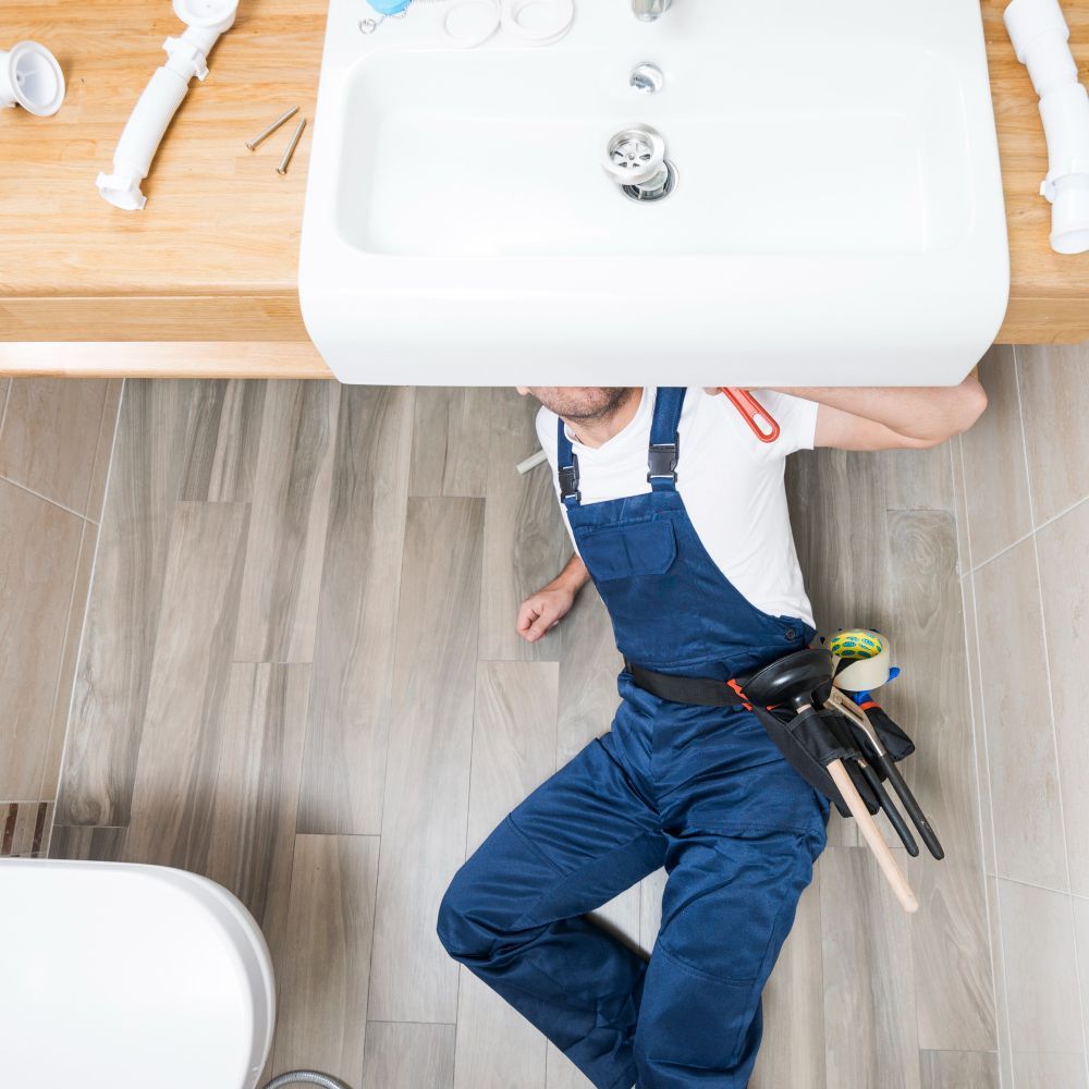 A plumber is laying on the floor under a sink in a kitchen.