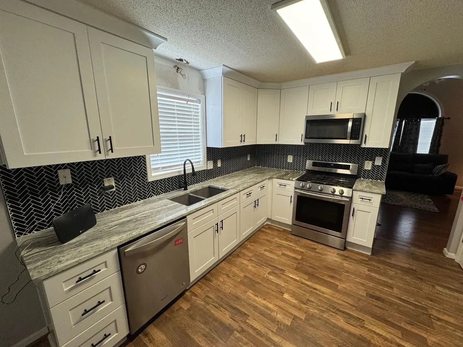 White kitchen with stainless steel appliances, herringbone backsplash, and wood floors.