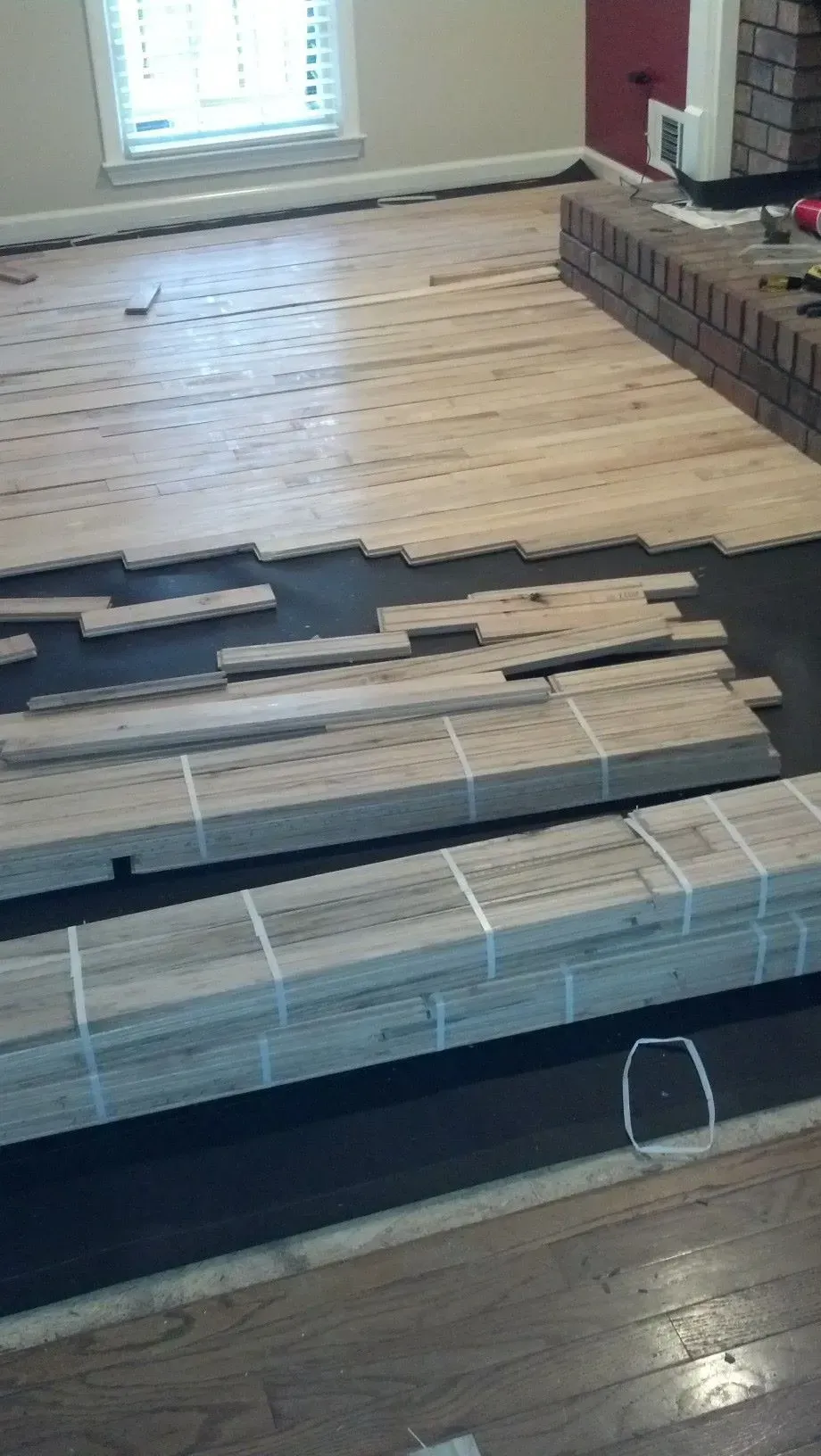 Wood flooring installation in progress, light wood planks laid on a dark underlayment.
