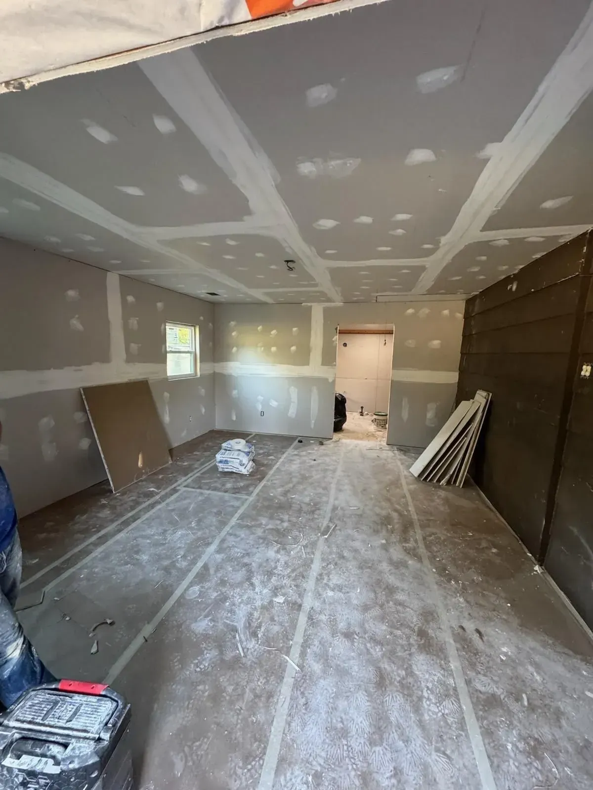 Interior room under construction, drywall installed on walls and ceiling, tape and mud applied.
