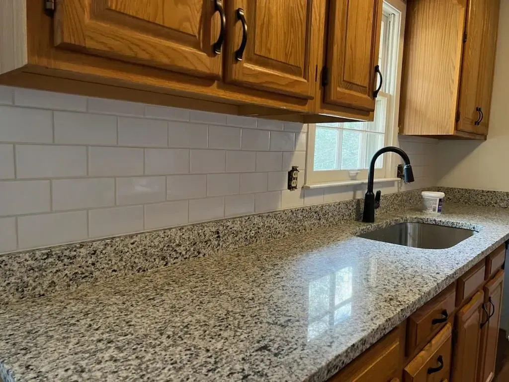 Kitchen counter with granite surface, white subway tile backsplash, and wooden cabinets.